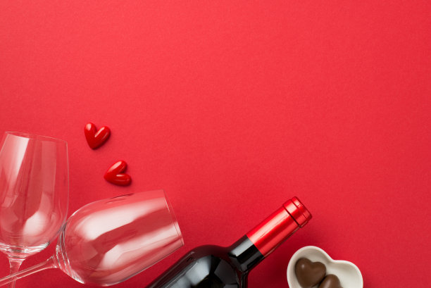 情人节装饰品的俯视图照片小心在两个葡萄酒杯之间，心形碟子上有巧克力糖果和酒瓶在孤立的红色背景与空白的空间图片下载