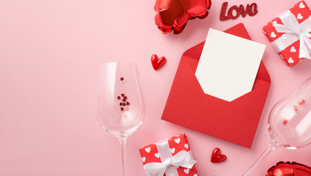 顶视图照片信封卡礼品盒在红色包装纸与图案的心题字爱，葡萄酒杯，五彩纸屑心形气球孤立柔和的粉红色背景与copyspace图片下载