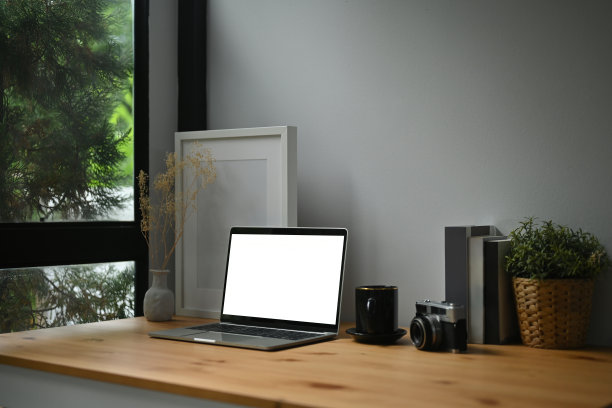 一张舒适的工作场所的照片，周围是白色的空白屏幕电脑笔记本电脑，空的相框，柳条篮子，老式相机，咖啡杯，罐子和书。图片下载