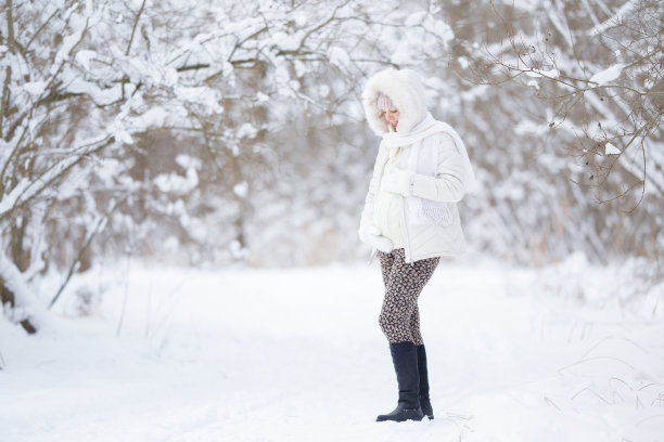 在白雪覆盖的自然公园里，穿着暖和衣服的孕妇戴着连指手套抚摸着大肚子。美丽寒冷的冬日。怀孕期间的动人时刻。孩子的期望。图片下载