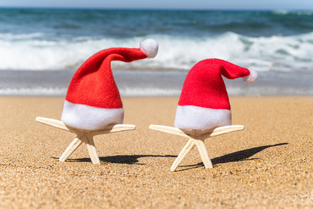 圣诞老人帽上的两个海星游客在沙滩上与海水背景。新年情侣度假概念图片下载