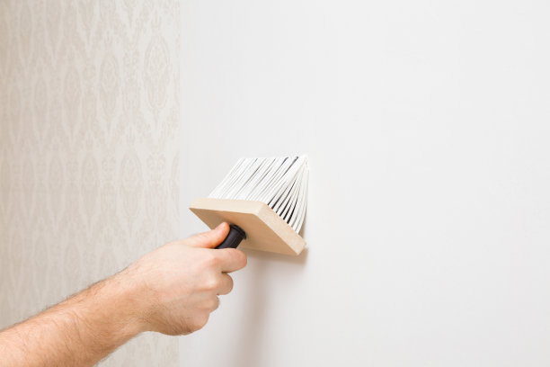 年轻的成年男子手用刷子在白色墙壁上涂胶水做壁纸。特写镜头。家居维修工作。侧视图。图片下载