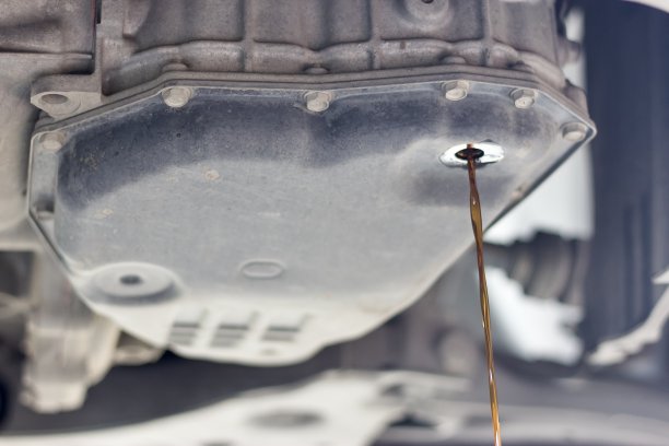 在泰国当地的小型汽车修理厂，当汽车在维修程序下进行换油时，乘用车肮脏的旧传动系统油落入集装箱的画面图片下载