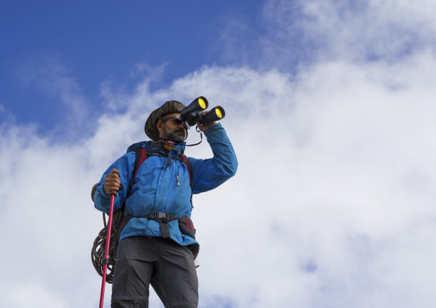 登山者通过双筒望远镜在山顶的云层上欣赏壮观的景色图片下载