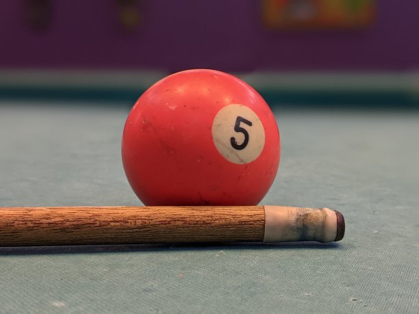 一个红色的台球和一个破旧的台球棍的特写照片，表面已经不再光滑，并印有数字5图片下载
