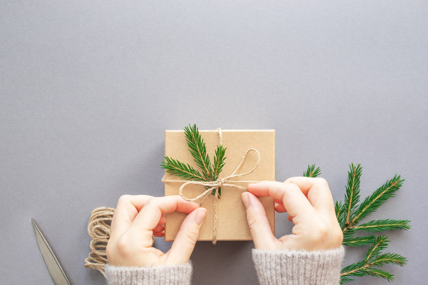 女性的手在灰色的背景上装饰一个圣诞礼盒、绳子和云杉树枝。零浪费，无塑料。平面，复制空间，俯视图。图片下载