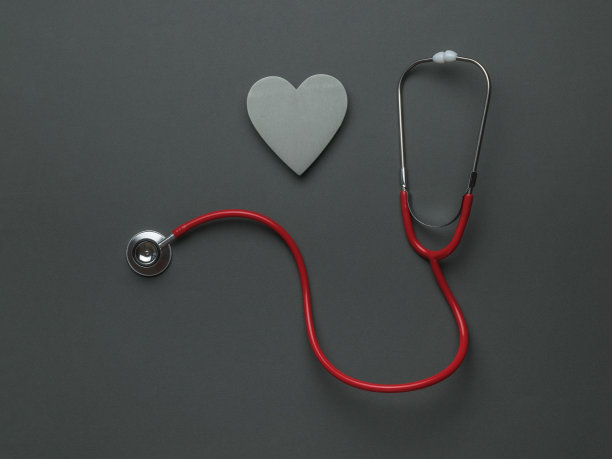 一个红色的听诊器和一个灰色的木制心脏在深灰色的背景上。医学检查的概念。图片下载