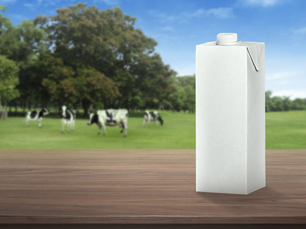 深色木质桌面的牛奶包装盒和草地上模糊的奶牛景观。健康饮食。乡村风格。空间设计图片下载