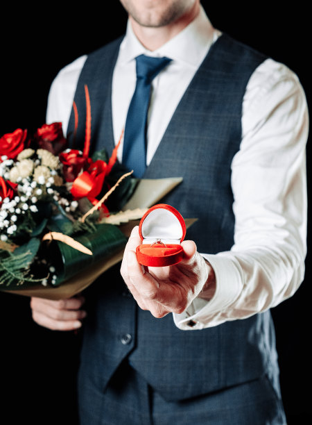 钻石戒指求婚。年轻幸福的男人捧着红色的礼盒，里面装着钻戒，红玫瑰花束。订婚结婚戒指。图片下载