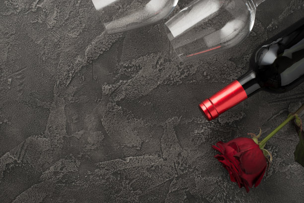 顶视图照片的saint valentine's day装饰两个葡萄酒杯，酒瓶和红玫瑰在孤立的纹理深灰色混凝土背景与空空间图片下载