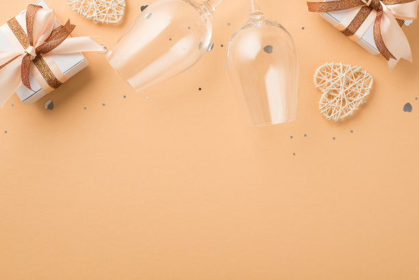 俯视图照片的情人节装饰两个葡萄酒杯藤心礼盒与发光的棕色和浅米色丝带蝴蝶结和亮片在孤立的米色背景copyspace图片下载