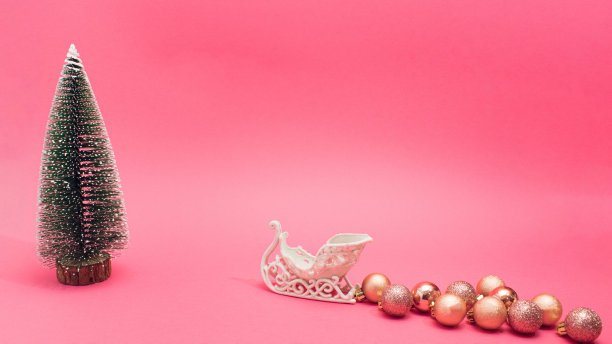 圣诞雪橇为新年带来礼物。复制空间与明亮的粉红色背景上的松树和装饰物。最小的节日气氛。素材图片