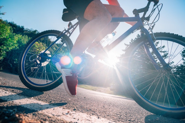 健康的男性自行车手骑他的自行车在柏油路在日落时，当太阳下山通过他的车轮。图片下载