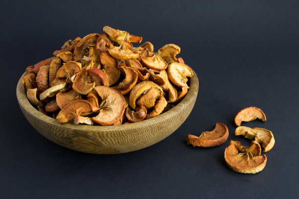 在黑色的背景上，在碗里放上切碎的苹果干。副本的空间。特写镜头。图片下载