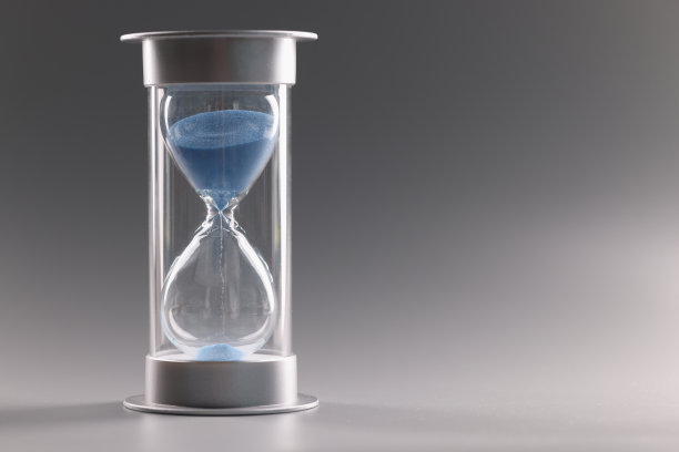 沙漏里装满了蓝色的沙子，沙子从小孔里流过图片下载