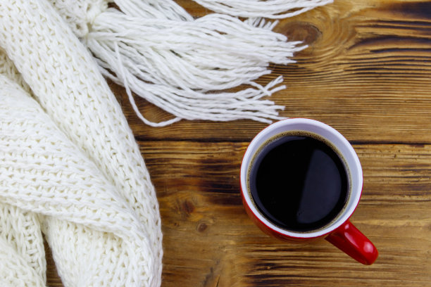 木桌上的白色针织围巾和咖啡杯。前视图。冬天舒适的概念图片下载
