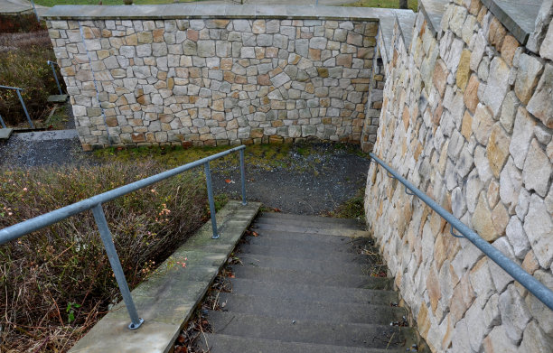 木板栅栏沿着几处出现裂缝的砂石墙、地形的运动和高速公路汽车交通的振动而建。绿草如茵的坡和高坡下的墙图片下载