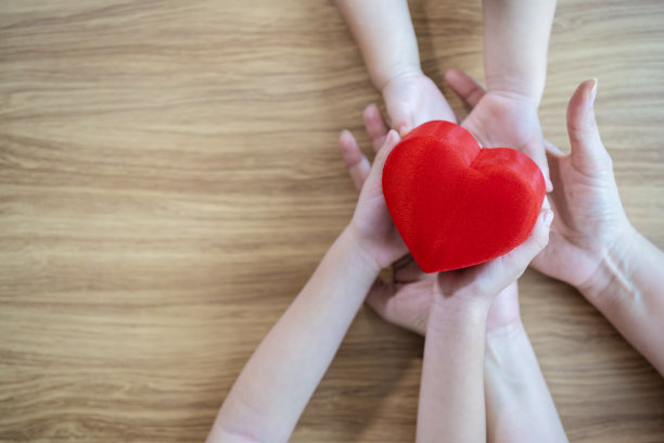 红色的心在孩子和母亲的手木制背景。爱的概念，慈善，同理心图片下载