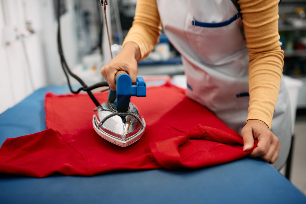 在纺织厂工作的妇女熨烫衣服的特写。图片下载