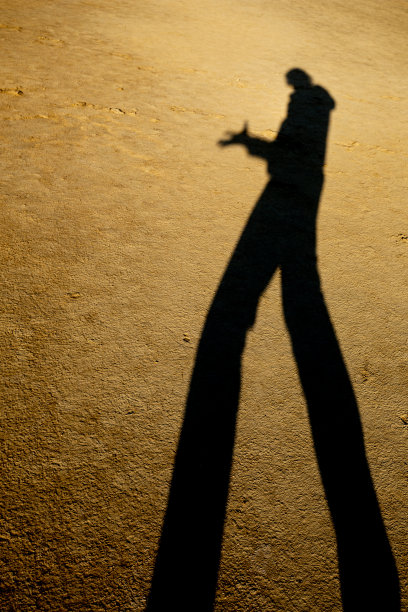 在贝尔卡泥火山保护区，细长的男人影子投射在一片被夕阳染黄的干泥地上图片下载
