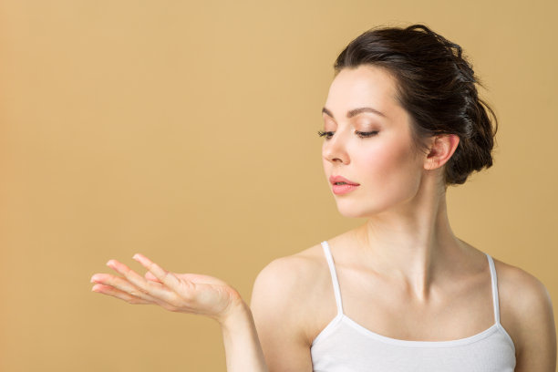 一个美丽的黑发女人的肖像与完美的皮肤。水疗女孩显示空的复印空间在打开的手掌为文本。提出了一种产品。美容Spa广告手势图片下载