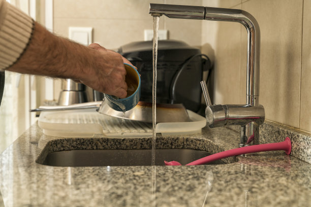 在厨房水槽里洗杯子和盘子的男人。图片下载