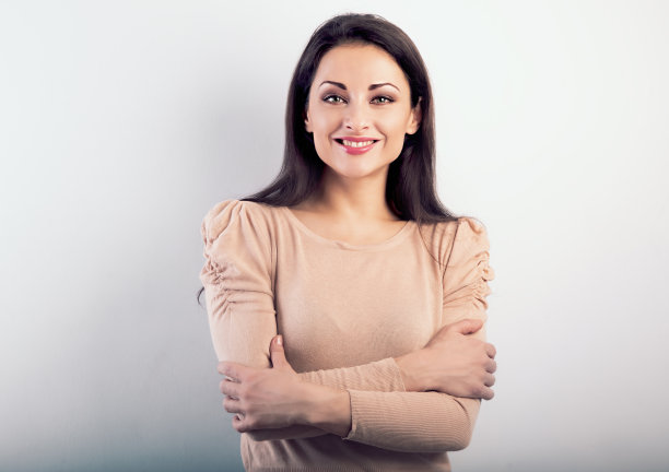 美丽自信可爱牙齿微笑的女人拥抱你自己与折叠的手臂在米色的衬衫蓝色的背景。特写肖像图片下载