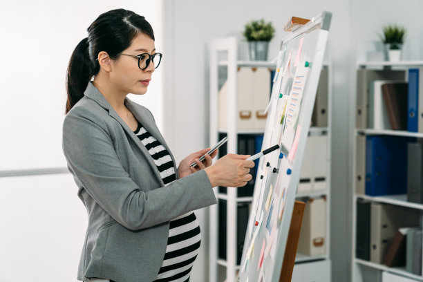 阳光明媚的创意办公室里，一名亚洲准女商人拿着手机指着统计数字，独自思考着经营战略。图片下载