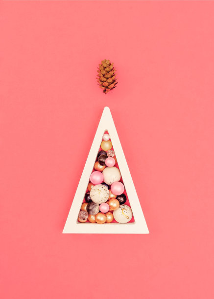 摘要圣诞树的概念。一个木制的白色三角形，上面有彩色的球。大理石和珍珠球。松果圣诞树顶状的松果珊瑚的背景。带有柔和阴影的概念。图片下载