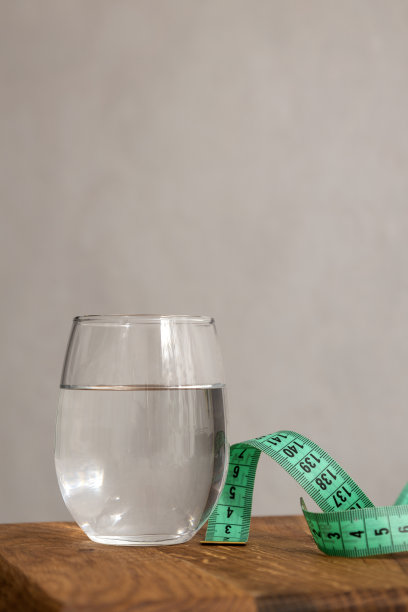 在明亮的墙面上，木制的桌子上摆放着清水玻璃和绿色的卷尺。空的空间图片下载