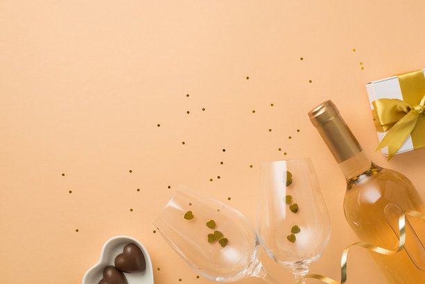 顶视图照片的情人节装饰礼盒与金弓心形碟子与糖果，酒瓶，酒杯与五彩纸屑和亮片在孤立的粉彩米色背景copyspace图片下载