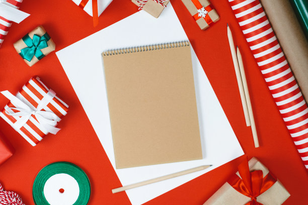 节日作文与拷贝空间。俯视图，平放礼品盒和包装纸卷与打开空白笔记本和铅笔写最好的祝福假期图片下载