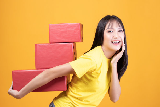 快乐微笑的女孩的肖像在随意地拿着礼品盒和表情脸孤立在黄色背景图片下载