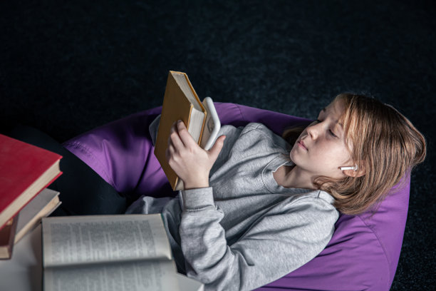 一个小女孩躺在沙发上用智能手机，而不是看书。图片下载