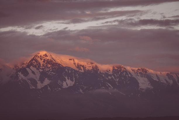 风景优美的山地景观，巨大的雪山山脉被黎明的太阳照射在低云之间。令人敬畏的高山风景，在日落或日出时高高的山脊。大冰川在顶部，复古的颜色图片下载