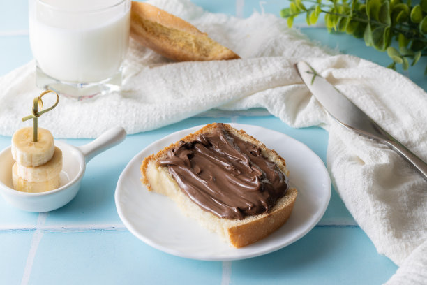 蓝色瓷砖背景上的巧克力酱、牛奶和香蕉片三明治图片下载