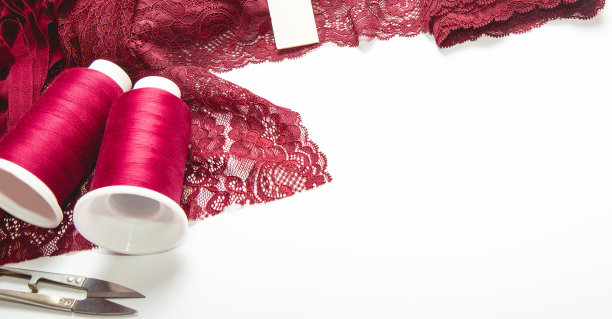 时尚背景。红色，酒红色花边织物，线程和各种设计师配饰在白色的桌子上，俯视图。空间的文本图片下载