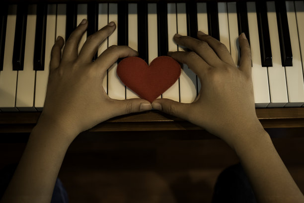 两只手握着键盘钢琴上的红色卡通心，告诉爱学习音乐或告诉某人爱。图片下载