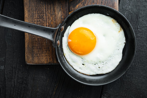 煎蛋与材料在铸铁煎锅，在黑色木桌背景，俯视图平躺图片下载