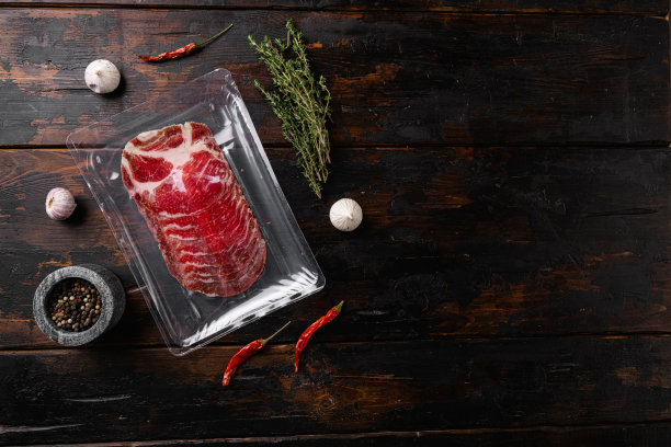 真空包装固化的coppa火腿，在旧的深色木制桌子背景上，俯视图平躺，与文本的拷贝空间图片下载