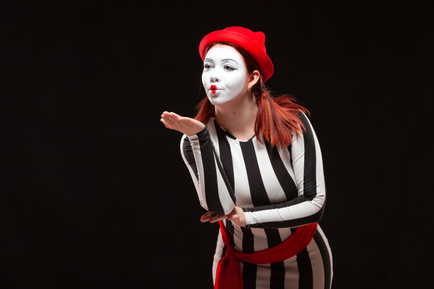 女哑剧艺术家表演的肖像，孤立在黑色背景上。一名身着条纹裙的女子摆出飞吻姿势图片下载