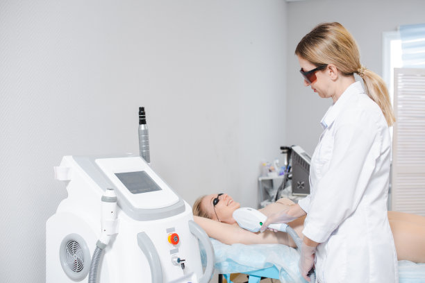 照片的一个现代美容设备和一个女皮肤科医生在保护眼镜进行手术激光脱毛的腋窝的一个年轻的女孩图片下载