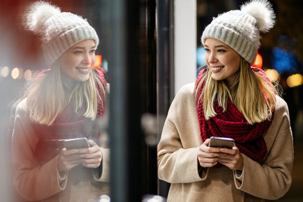 年轻美丽的女人用她的手机上网在冬天的一天在城市图片下载