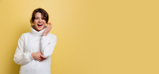 传单与开朗的年轻美丽的女孩在温暖的白色针织毛衣笑孤立在黄色的背景图片下载