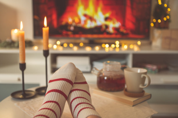 旁边的桌子上放着穿着条纹袜子的脚的照片，上面有蜡烛、茶壶和杯子，还有壁炉仿品图片下载