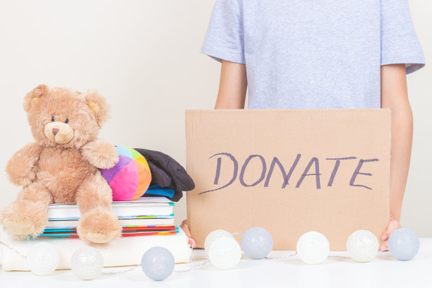 慈善捐赠。孩子的手拿着棕色的纸板，上面写着“捐赠”。志愿者收集儿童衣服，书籍和玩具捐赠图片下载