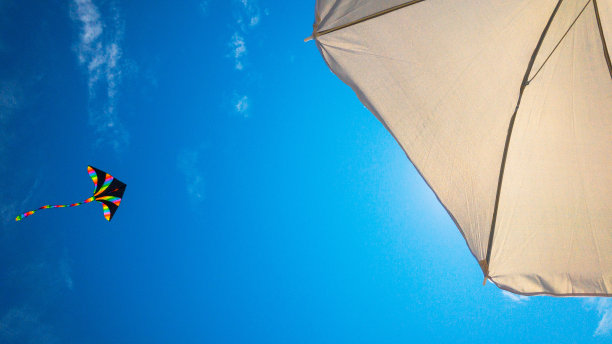 风筝的蓝天。五颜六色的高空飞行玩具。风筝在风云上飞翔。彩虹风筝在夏天的背景。梦想、自由、童年的概念。图片下载