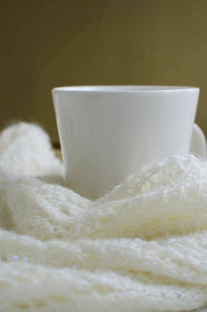 一杯热茶被裹在一条温暖的白围巾里。秋季背景与复制空间图片下载