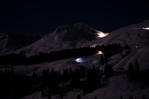 山村的斯图斯夜间与斜坡和照明雪炮喷洒人工雪与背景山的全景。图片下载