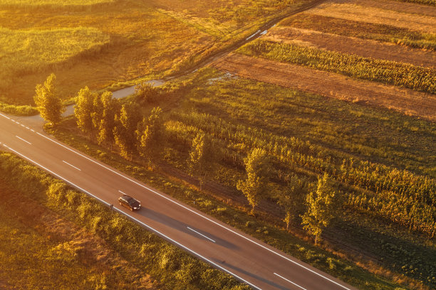 无人机拍摄的黑色轿车在夏日夕阳下行驶在路上图片下载